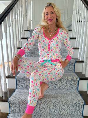 Woman sitting on a staircase wearing colorful birthday themed pajamas with a pattern of festive shapes.