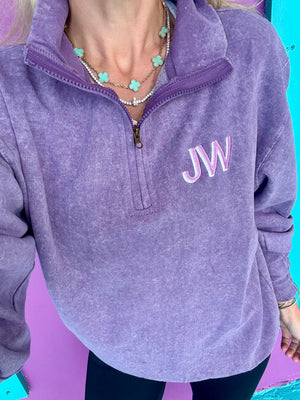 A purple quarter zip pullover with embroidered initials on the chest.