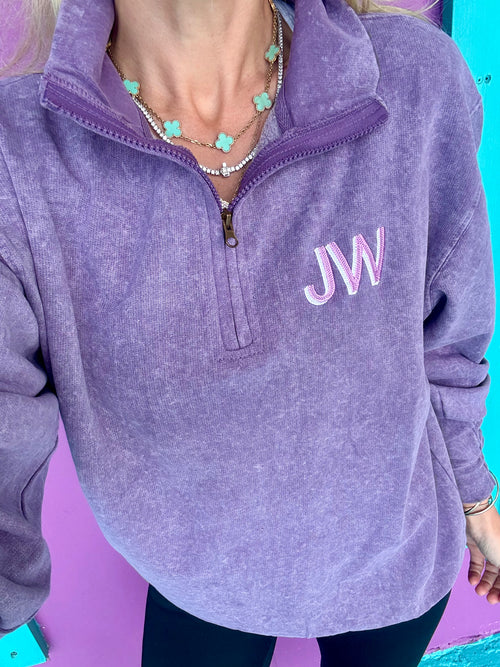 A purple quarter zip pullover with embroidered initials on the chest.