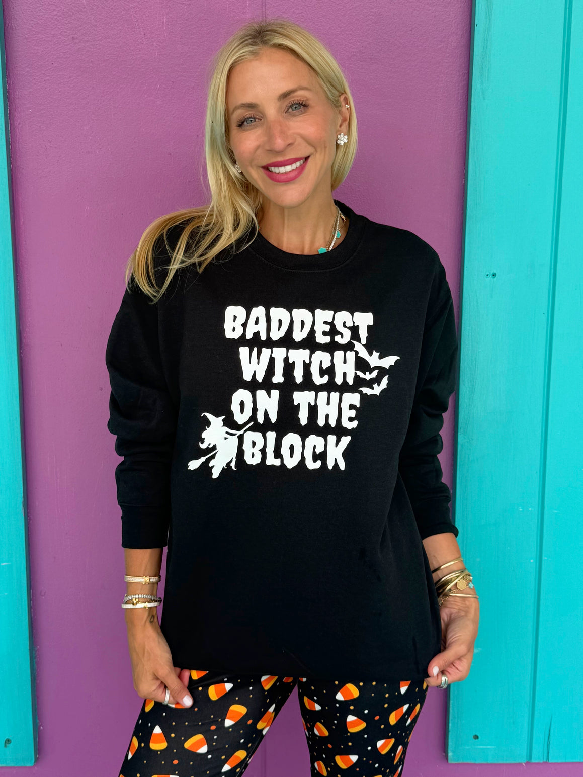 Woman wearing a black sweatshirt with 'Baddest Witch on the Block' text against a colorful background