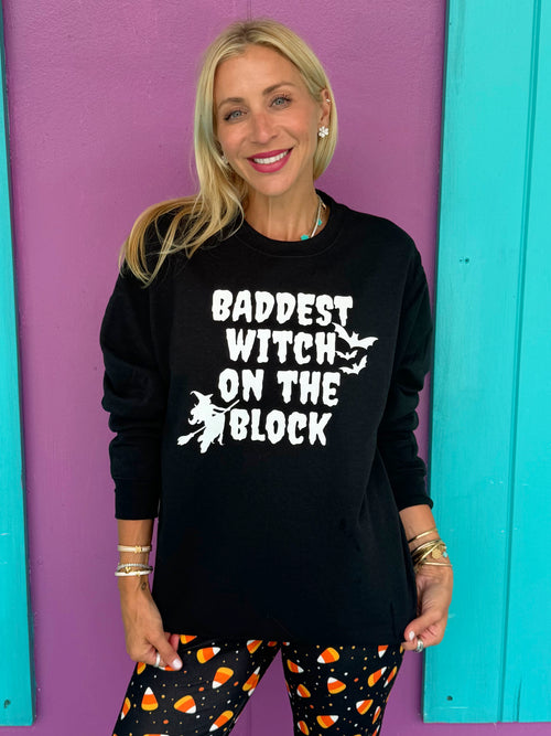 Woman wearing a black sweatshirt with 'Baddest Witch on the Block' text against a colorful background