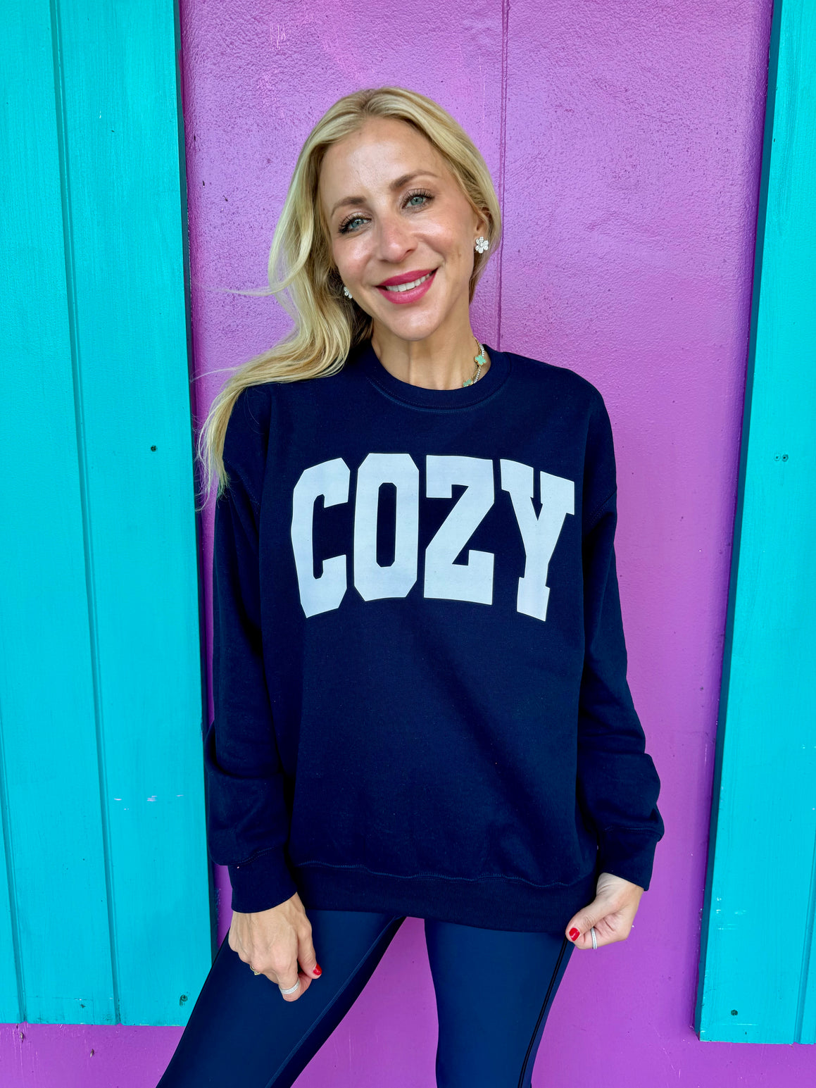 A woman wearing a navy blue sweatshirt with the word 'COZY' printed in white letters on the front.