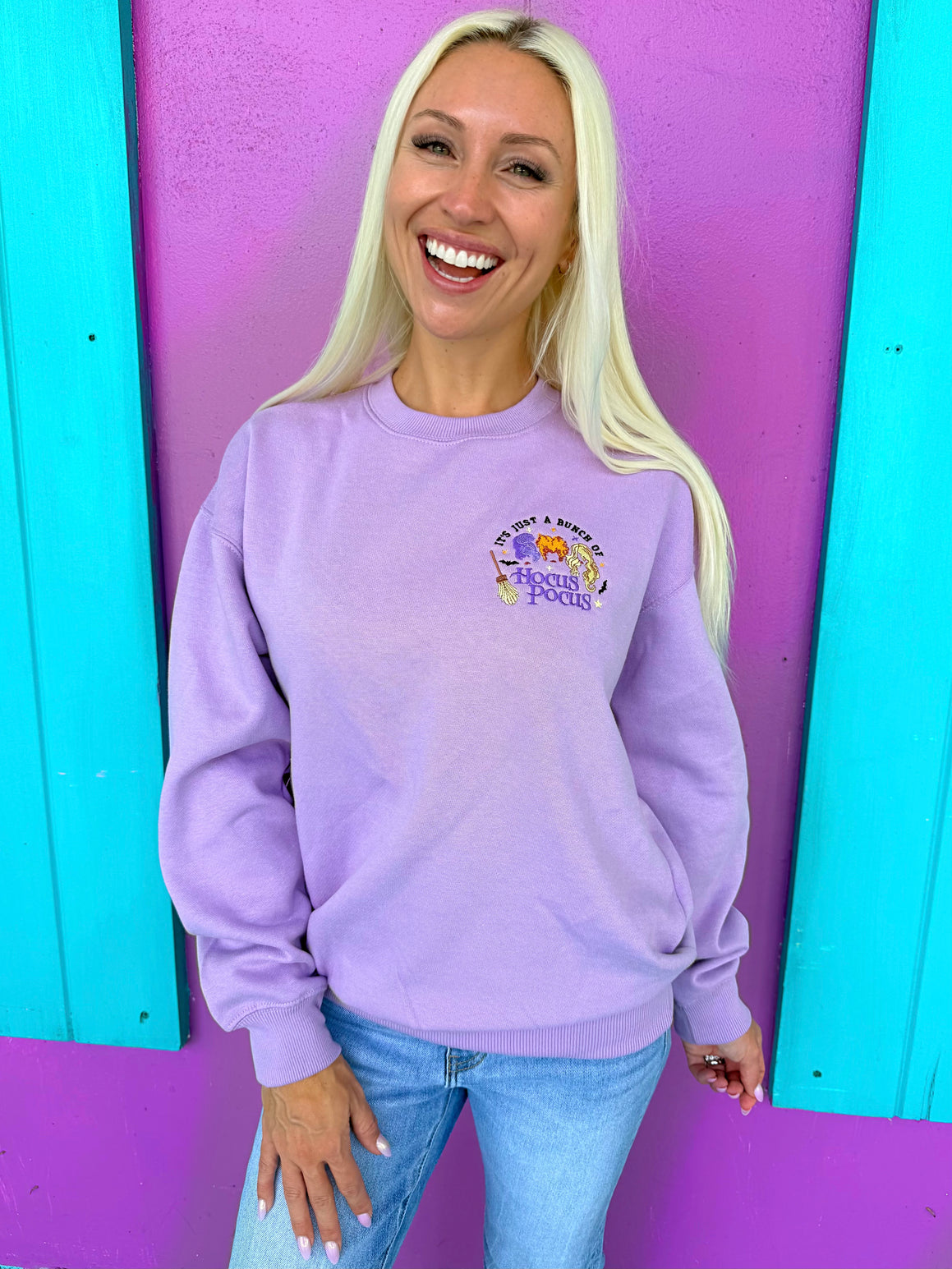 Woman wearing a purple sweatshirt with a colorful graphic design against a vibrant purple and blue background.