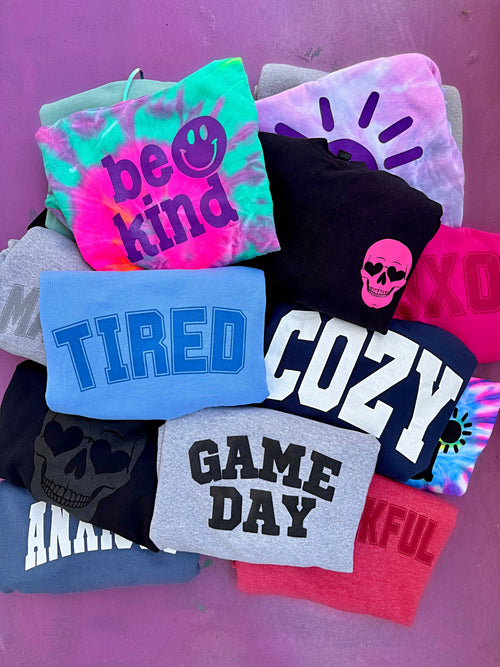 Collection of colorful sweatshirts with various designs and text on a purple background