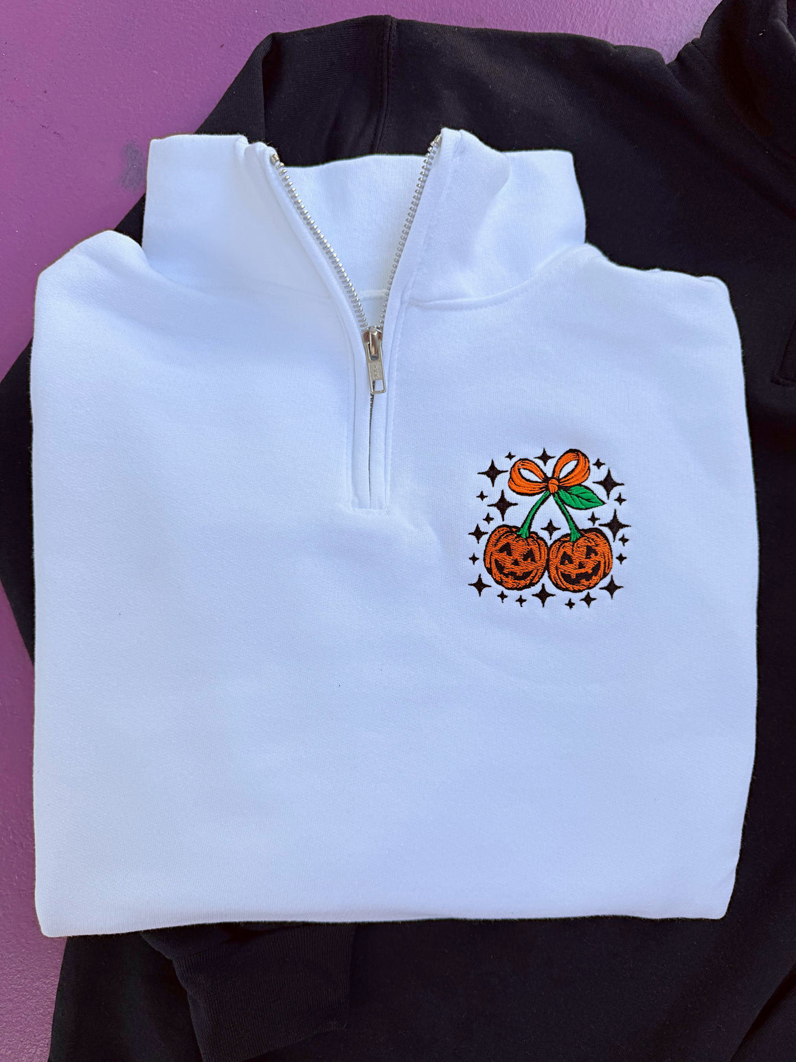 White quarter-zip sweatshirt with Halloween-themed design on a black background