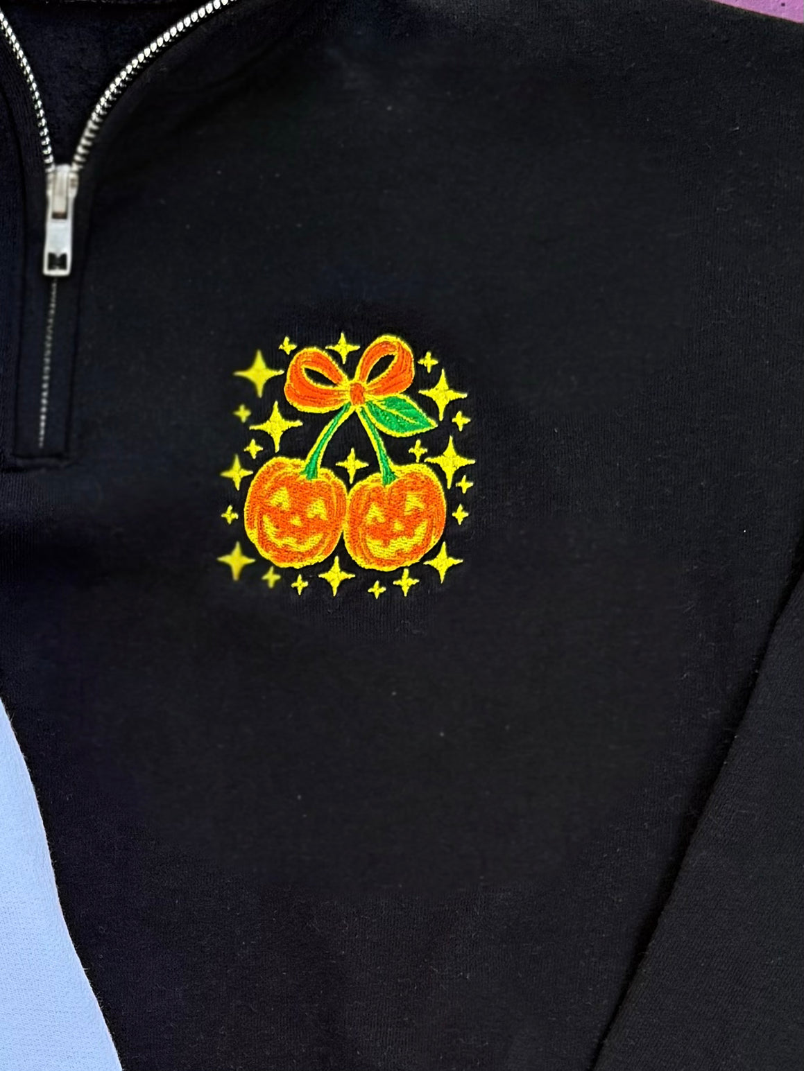 Black quarter-zip sweatshirt with Halloween-themed design featuring pumpkins and a bow.