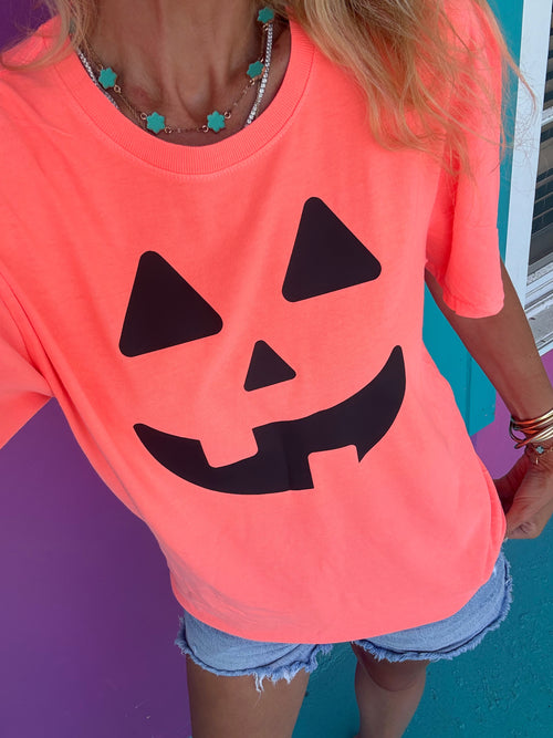 Person wearing a bright orange t-shirt with a black jack-o'-lantern face design against a colorful background.