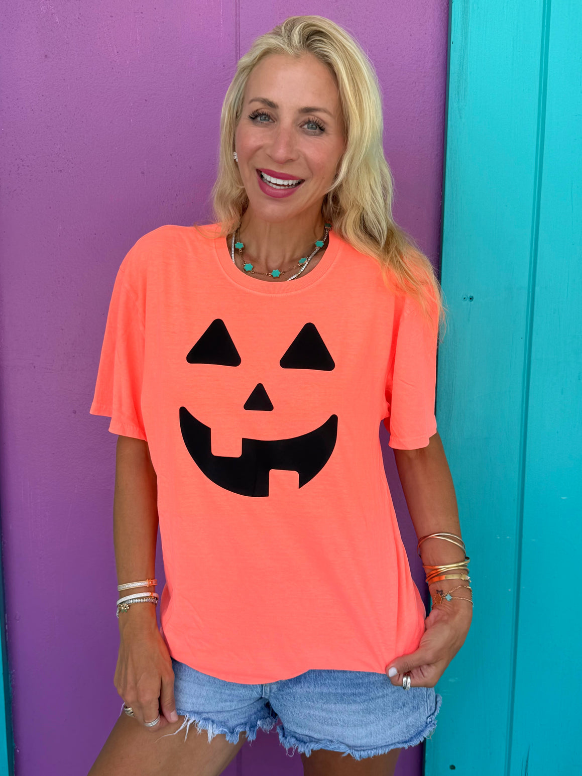 Woman wearing a bright orange t-shirt with a black jack-o'-lantern face design, standing against a colorful background.