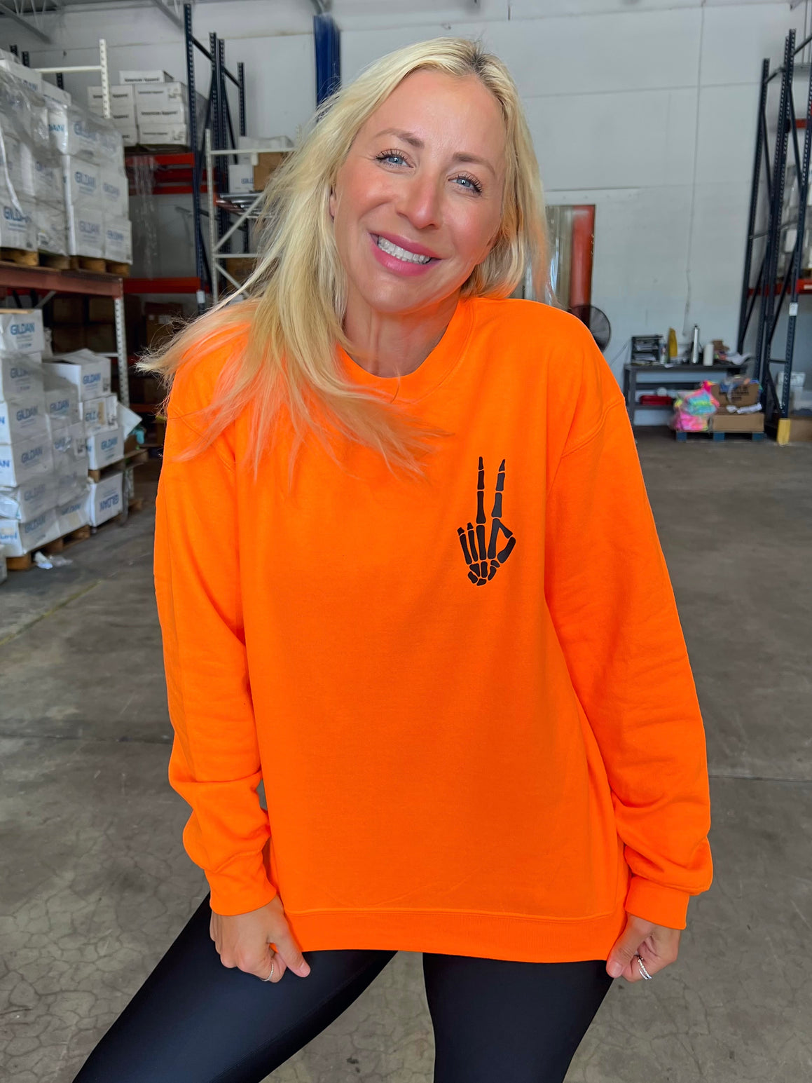 A person wearing a neon orange sweatshirt with a black skeleton hand screen-printed on the left chest area.