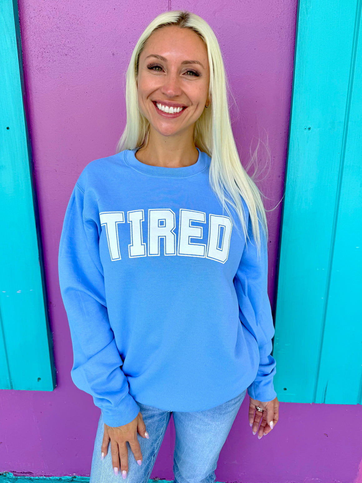 Woman wearing a blue sweatshirt with 'TIRED' text against a colorful background