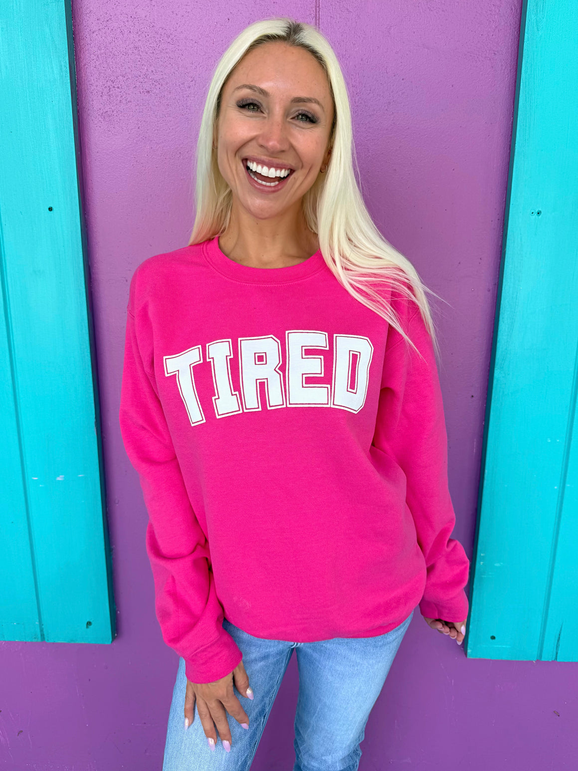 Woman wearing a pink sweatshirt with 'TIRED' text against a colorful background