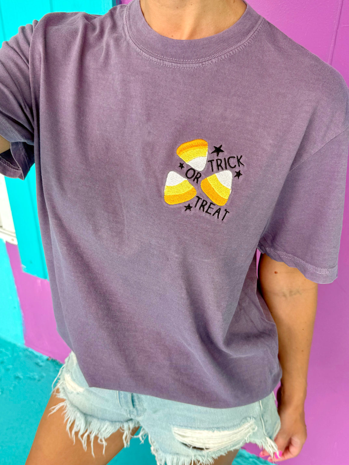 Person wearing a purple t-shirt with candy corn design and text on a colorful background