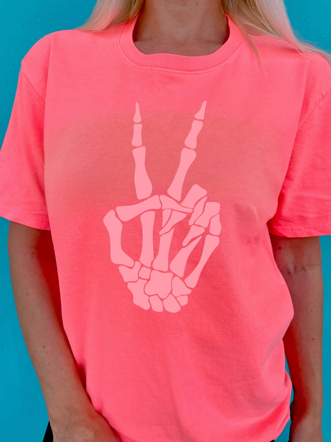 Person wearing a pink t-shirt with a skeleton hand peace sign design against a blue background