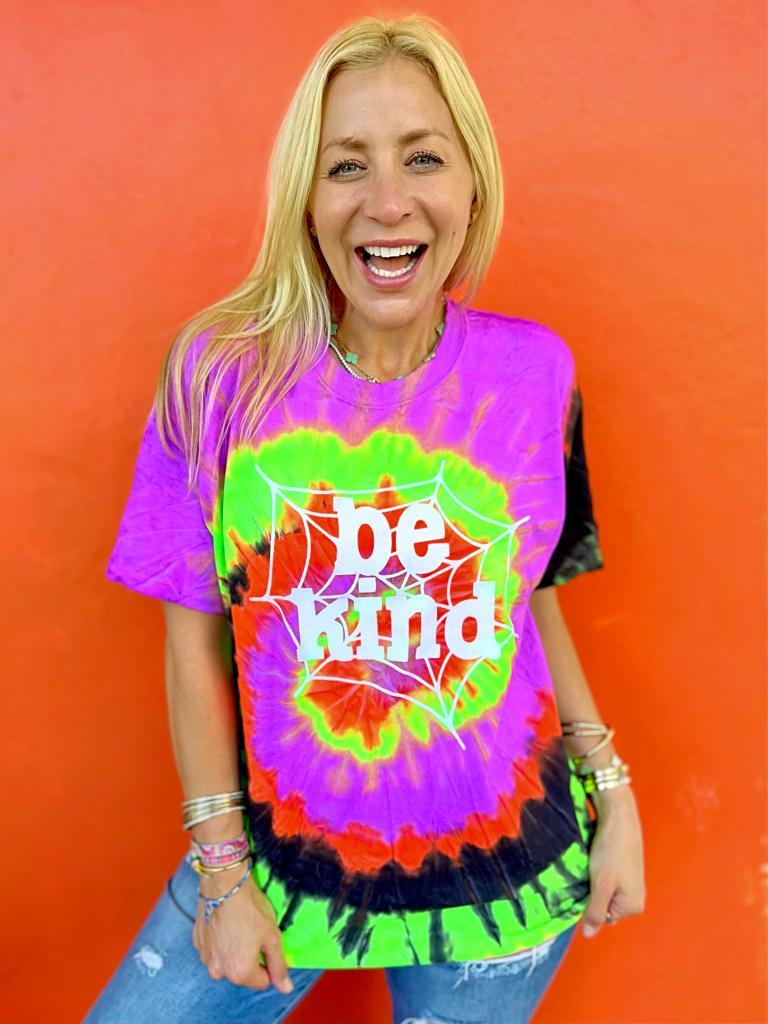 Person wearing a tie-dye shirt with 'be kind' text against an orange background

