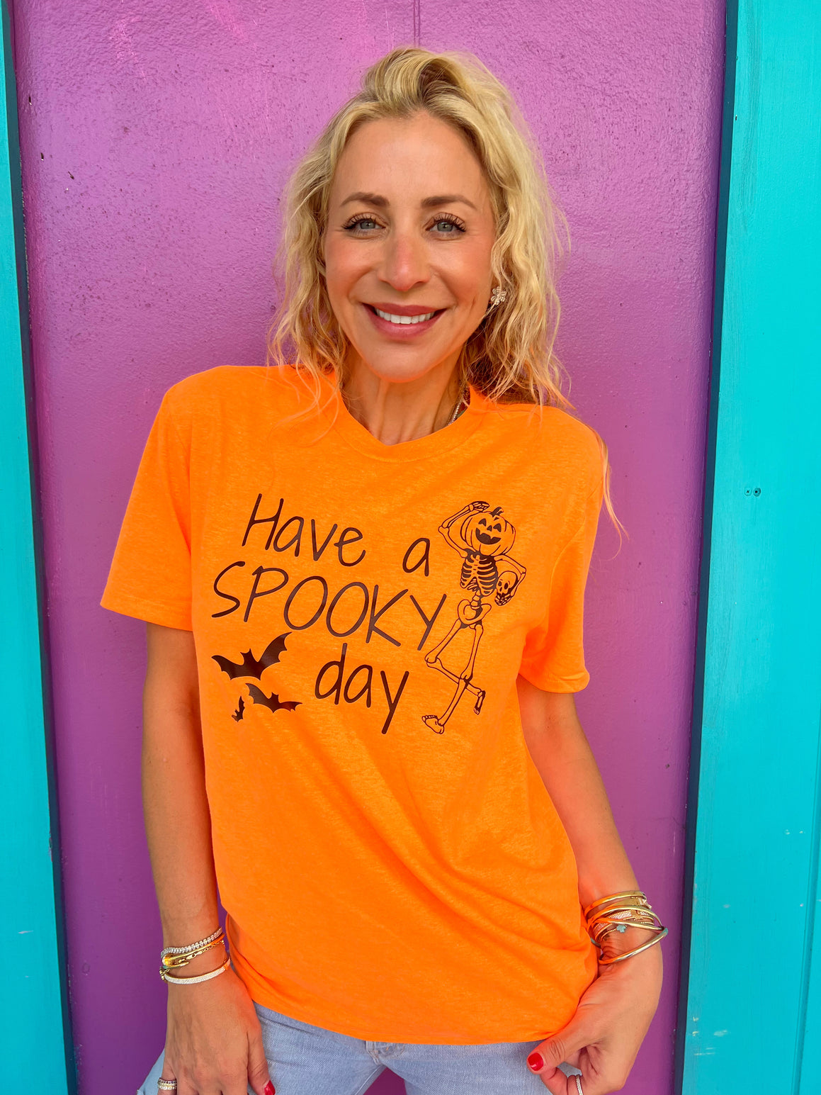 Woman wearing an orange t-shirt with Halloween text and graphics against a colorful background


