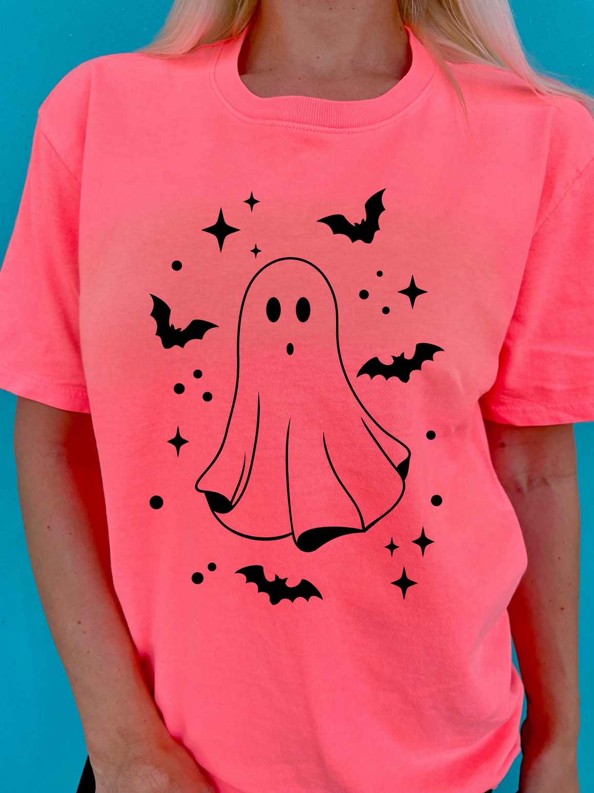 Person wearing a pink t-shirt with a ghost and bat design on a blue background